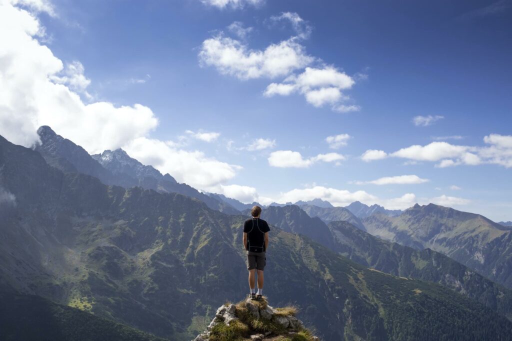 A hiker standing on a narrow mountaintop overlooking mountains